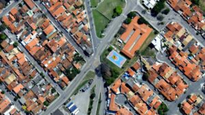 A imagem mostra um exemplo claro dos resultados obtidos por meio de aerolevantamento: uma captura aérea de alta resolução que permite visualizar com nitidez a malha urbana, incluindo ruas, quadras, construções e equipamentos públicos, como a quadra esportiva no centro da imagem.